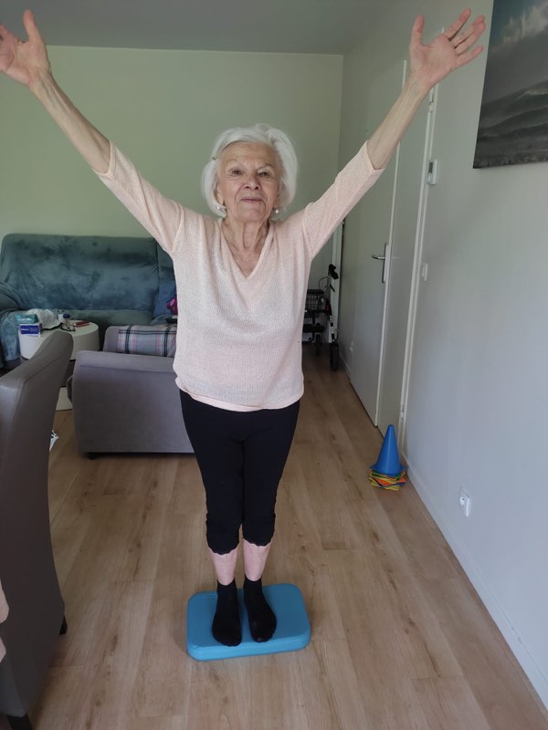 Cliente travaillant l'équilibre sur un coussin proprioceptif dans son salon