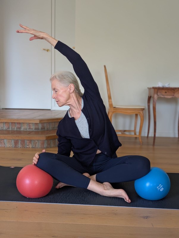 Cliente en travail de Pilates assis, appuis sur ballons souples, à domicile